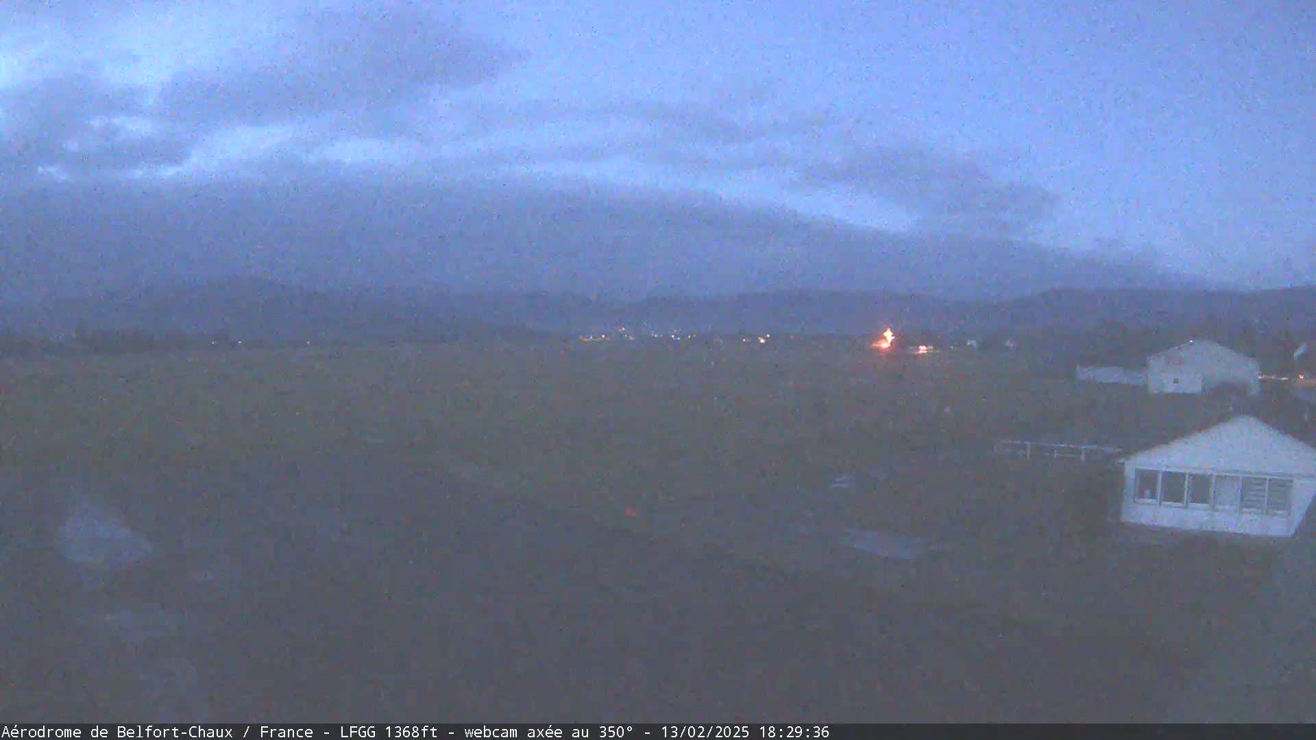 Under a dusky, overcast sky, a flat expanse of land is visible with a few houses and distant lights.