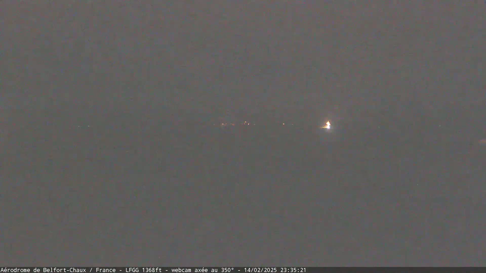A nighttime, dark gray outdoor scene shows a few distant lights on the horizon under a cloudy sky.
