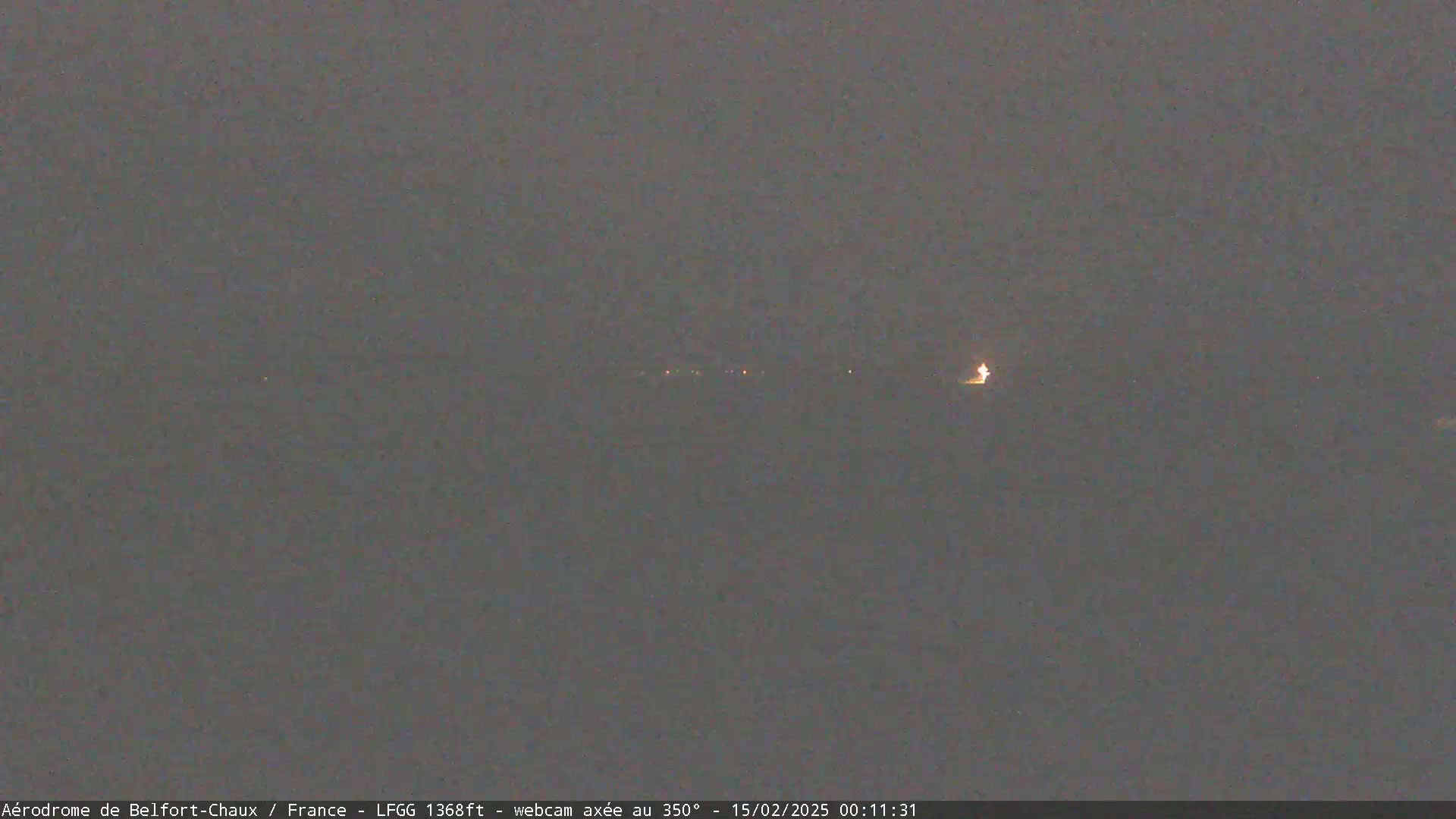 A dimly lit, dark gray landscape is visible at night, with a few faint lights in the distance.