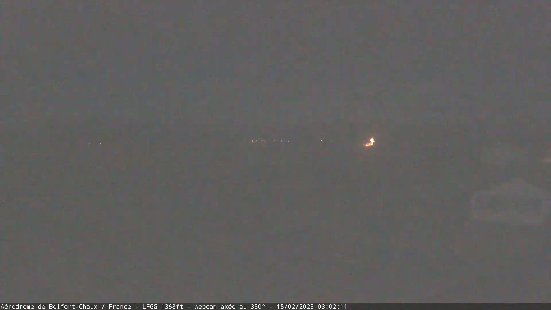 A dark, nighttime scene shows a few distant lights in the hazy distance.