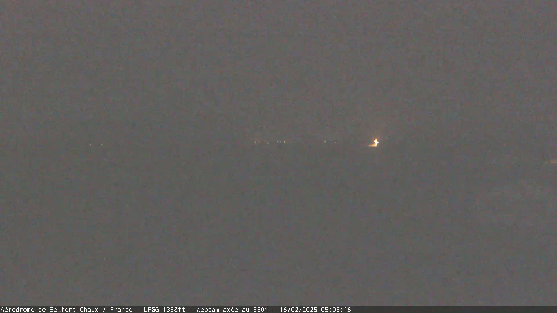 A dark, blurry nighttime scene shows a few faint lights in the distance under a gray sky.
