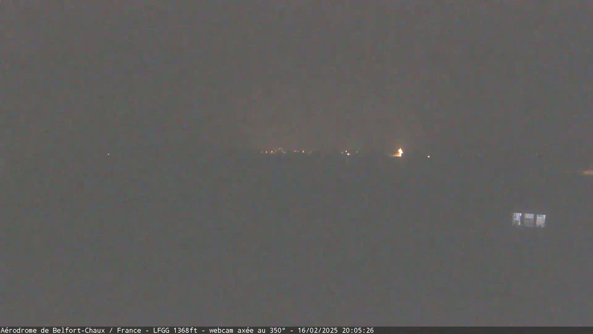 A dark, nighttime landscape is visible, showing a few faint lights in the distance under a cloudy sky.