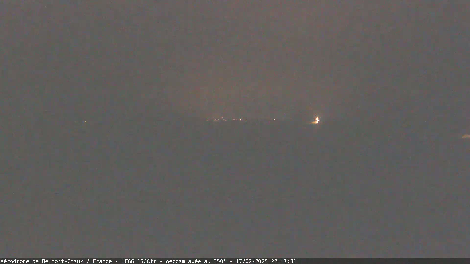 A dark, nighttime landscape is visible with a few faint lights in the distance under a cloudy sky.