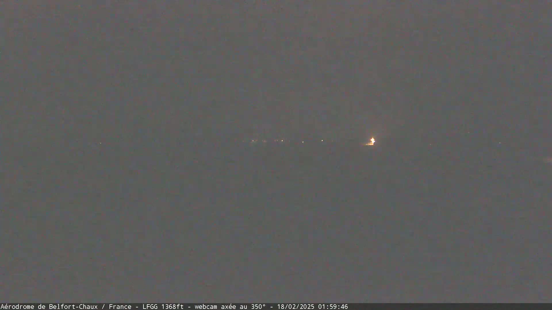 A dimly lit, dark landscape is visible at night, with a few faint lights in the distance.