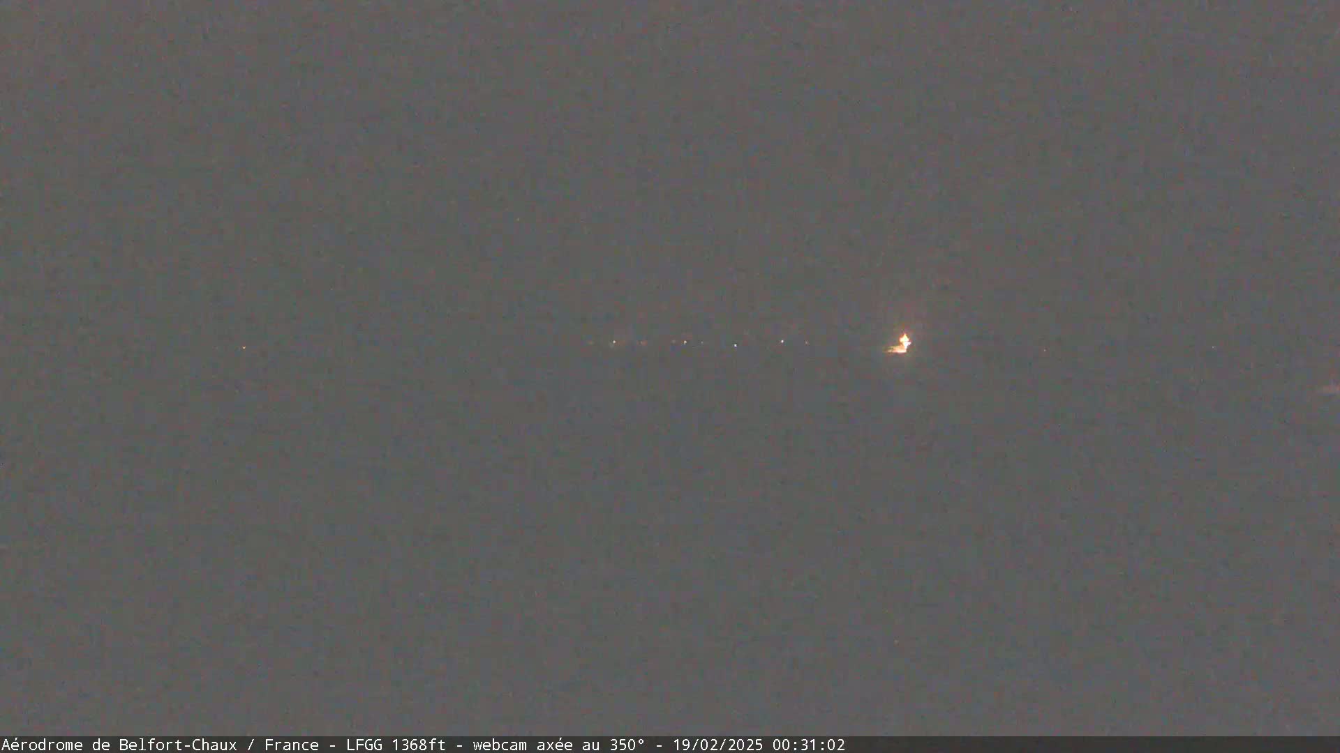 A nighttime long shot shows a line of faint lights on the horizon under a dark, overcast sky.