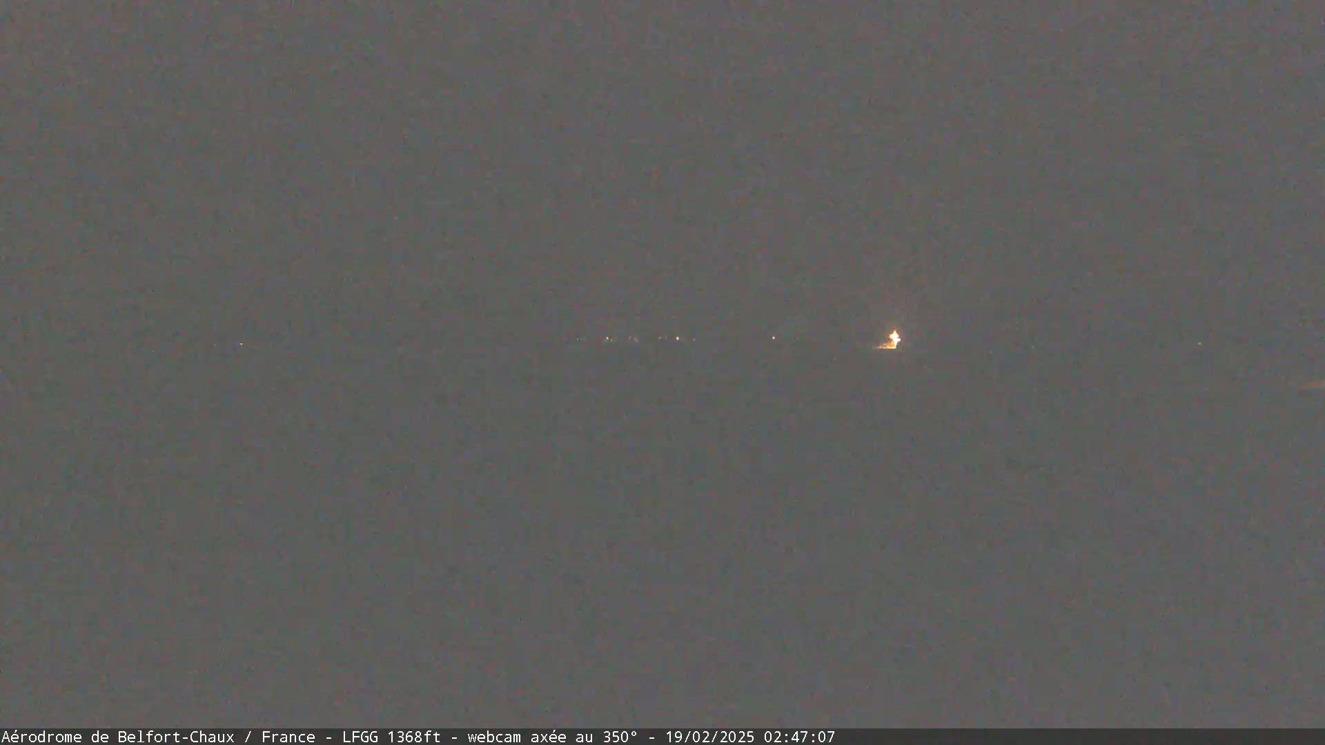 A dark, nighttime scene shows a line of distant lights on the horizon under a mostly clear, dark sky.