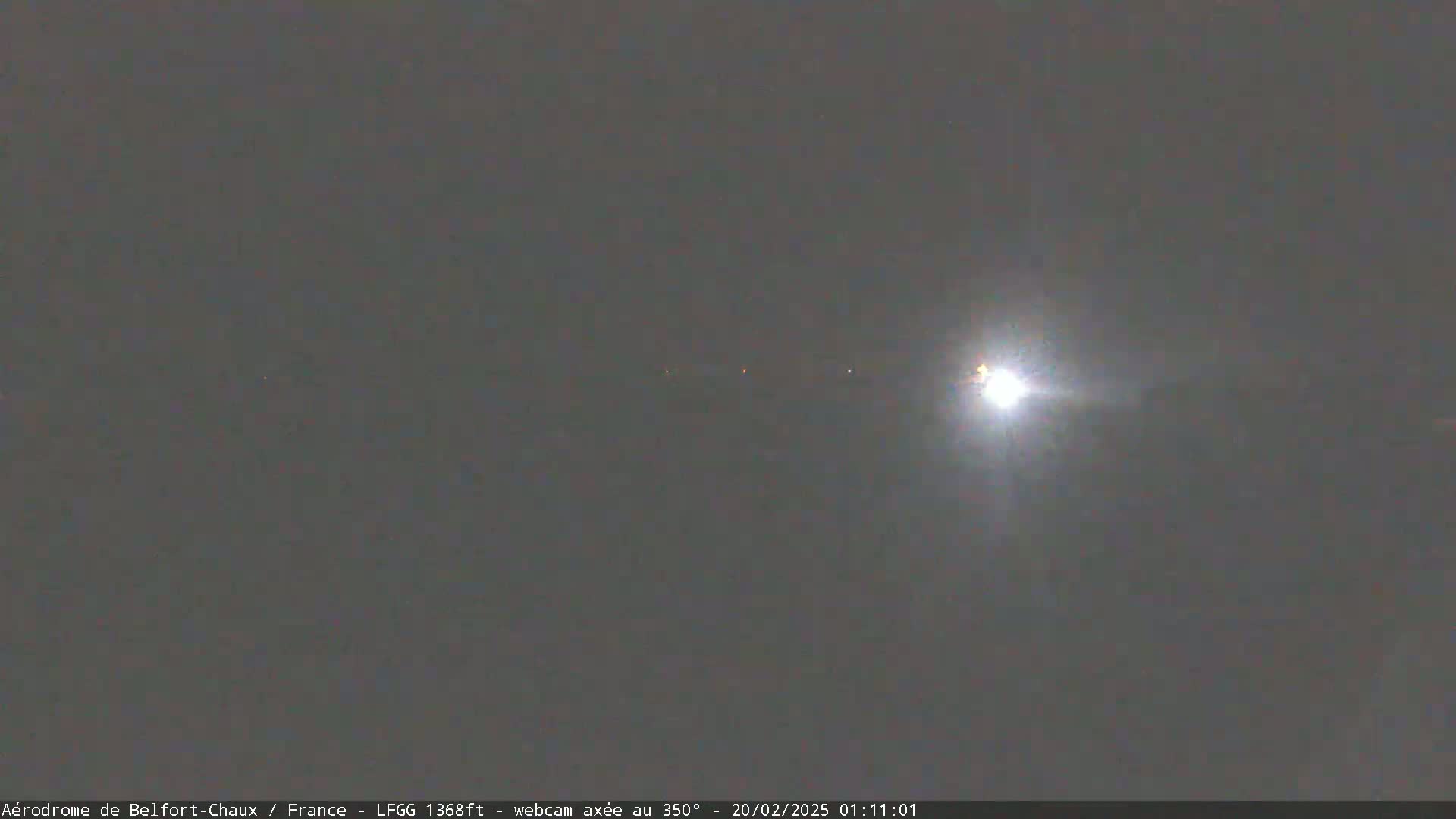 A bright light, possibly the moon, shines in a dark, overcast night sky.