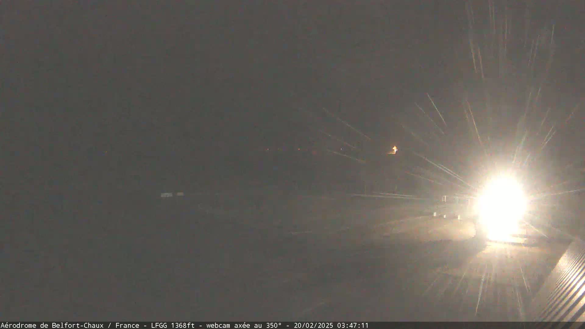 A bright light shines from a vehicle at night, in snowy conditions.