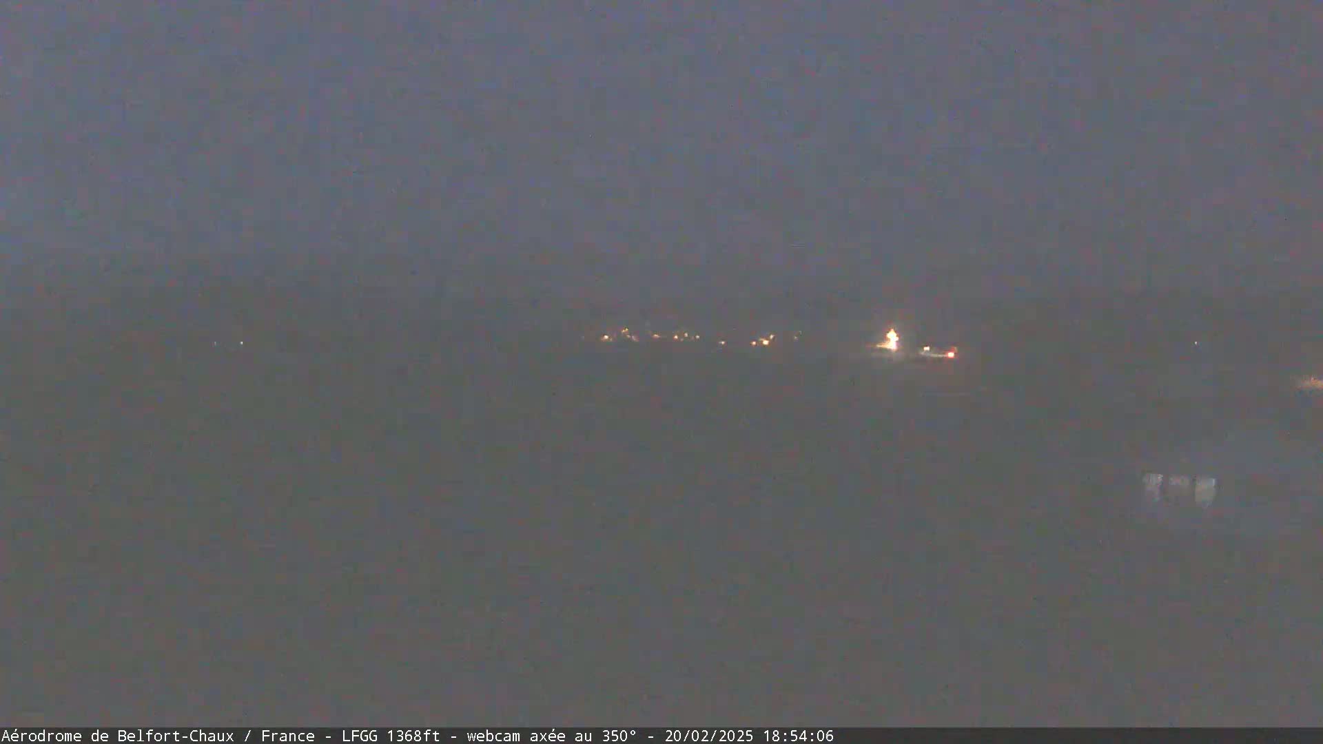 A blurry, dark image shows a distant line of faint lights at night under a hazy sky.