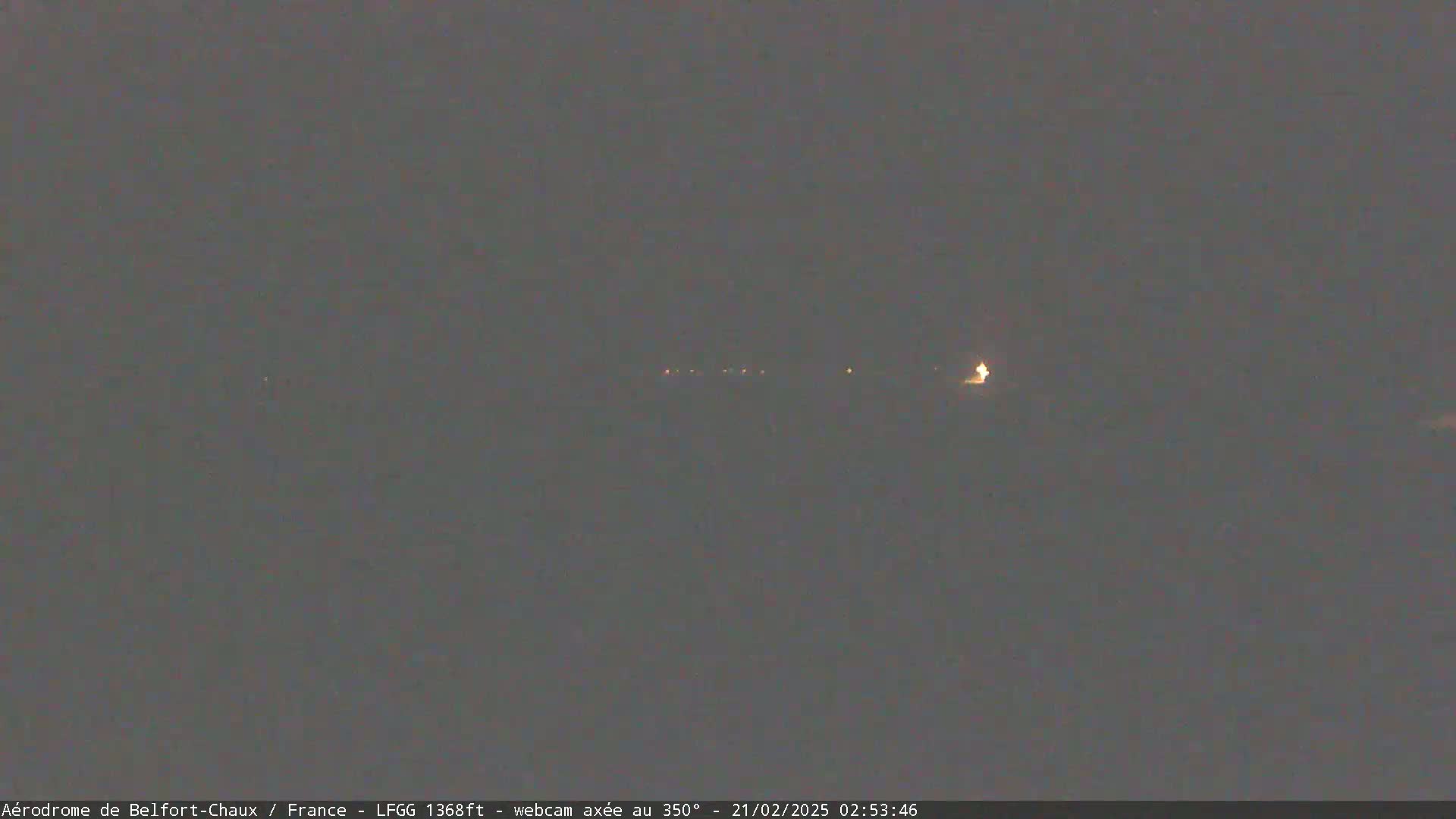 A dark, nighttime scene shows a few distant, faint lights on the horizon under a mostly clear sky.