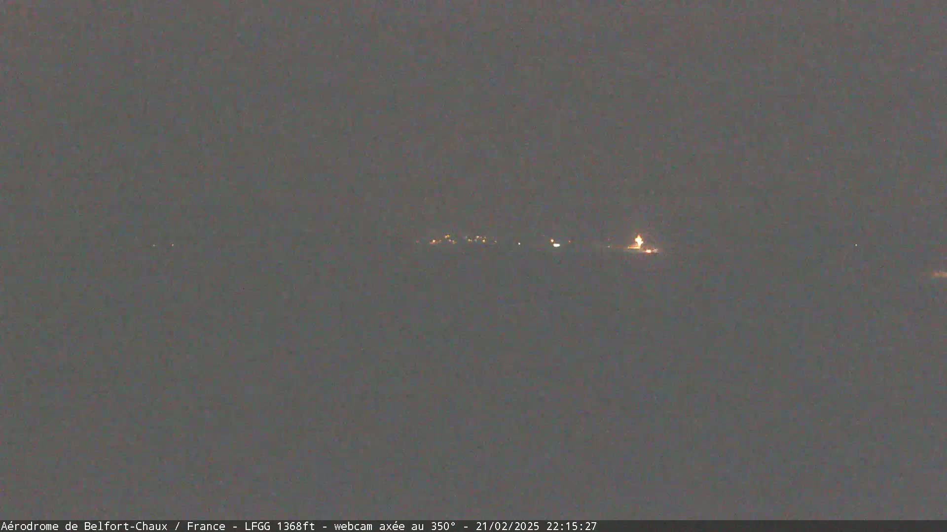 A dark, nighttime scene shows a few faint lights in the distance under a dark, overcast sky.