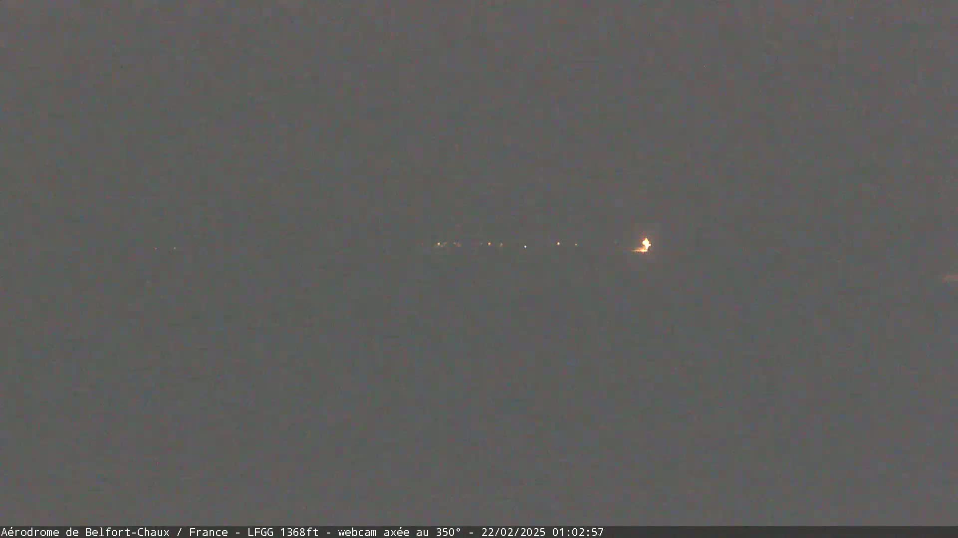 A dimly lit, nighttime landscape is visible, showing a few faint lights in the distance under a dark sky.