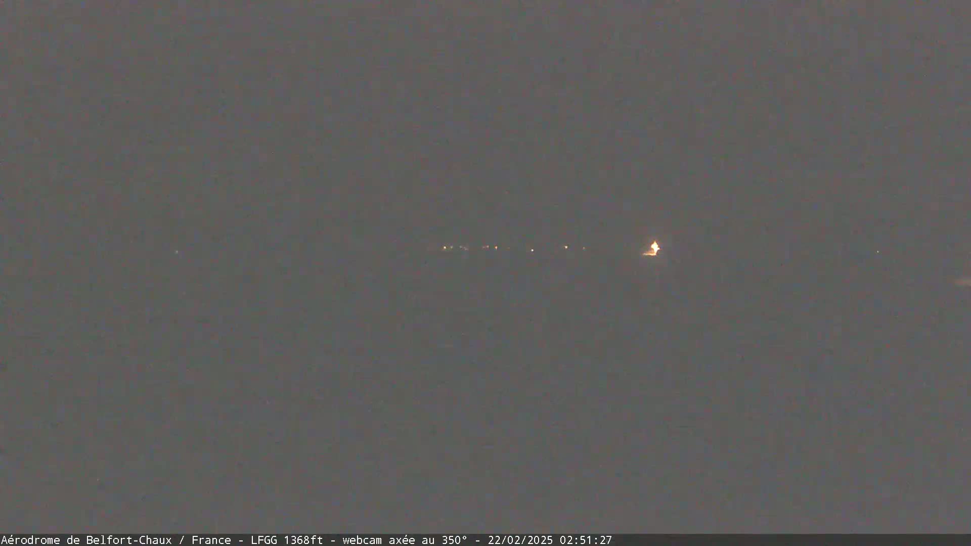 A nighttime long shot shows a dimly lit landscape with a few distant lights under a dark, overcast sky.