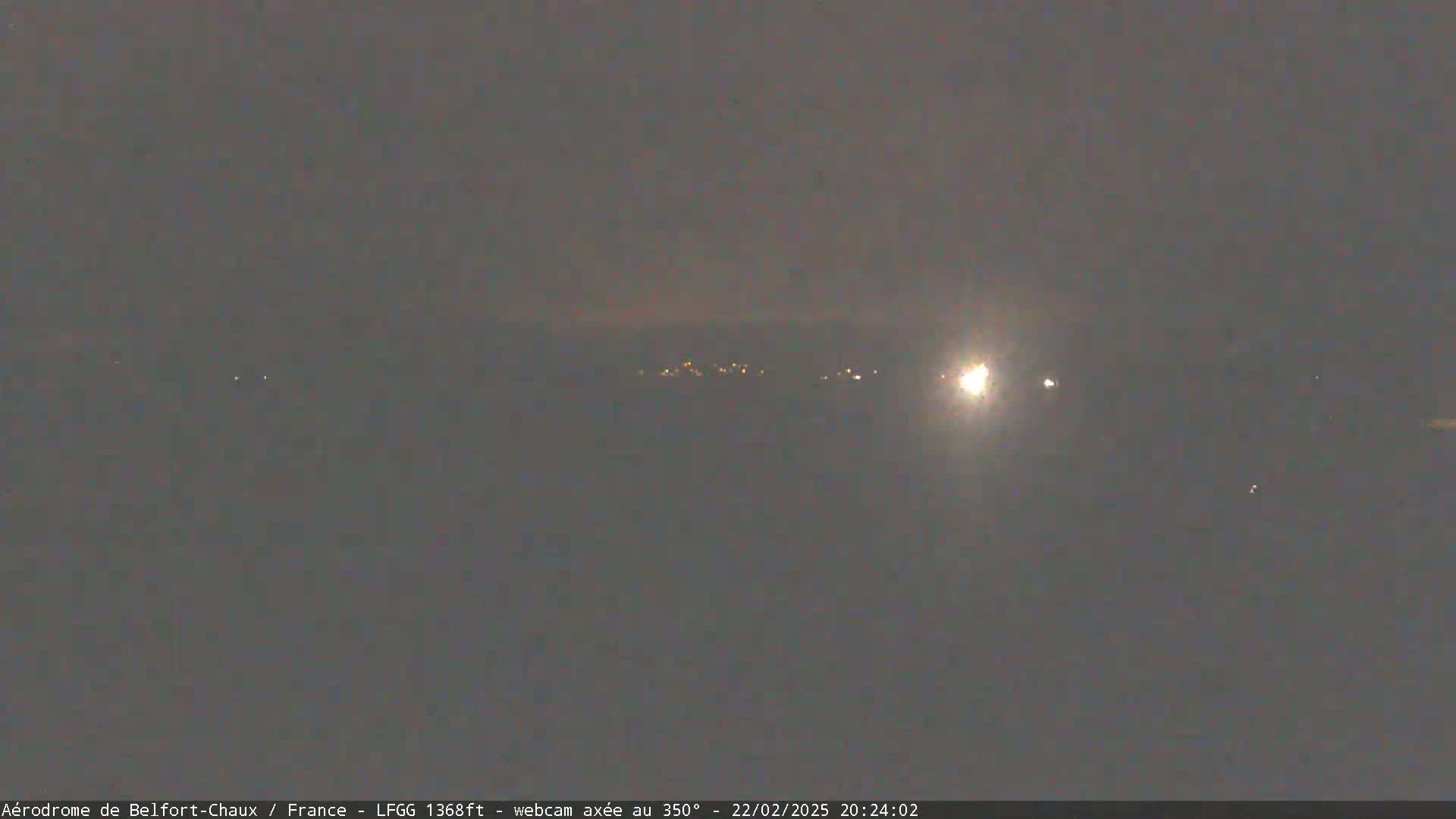 A nighttime, hazy view shows a distant line of lights, possibly a town or village, with a bright light source in the mid-right distance.