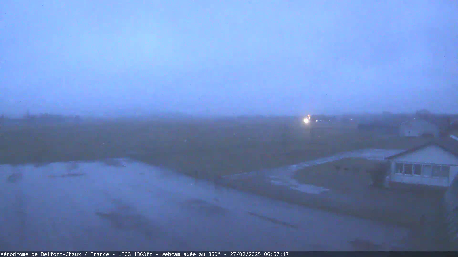 A foggy, twilight scene shows a flat landscape with a few houses and a road, partially flooded in the foreground.