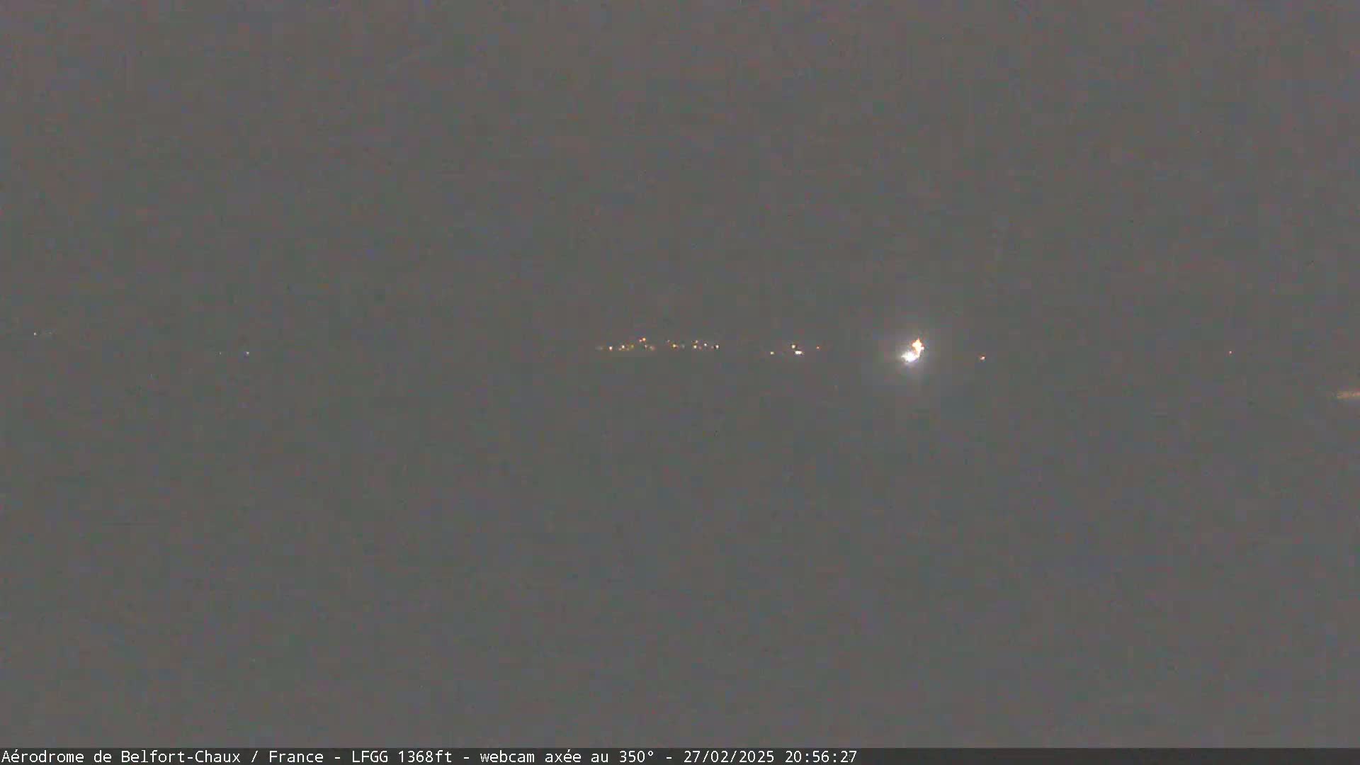 A dark, nighttime landscape shows a distant line of faint lights under a mostly clear sky.