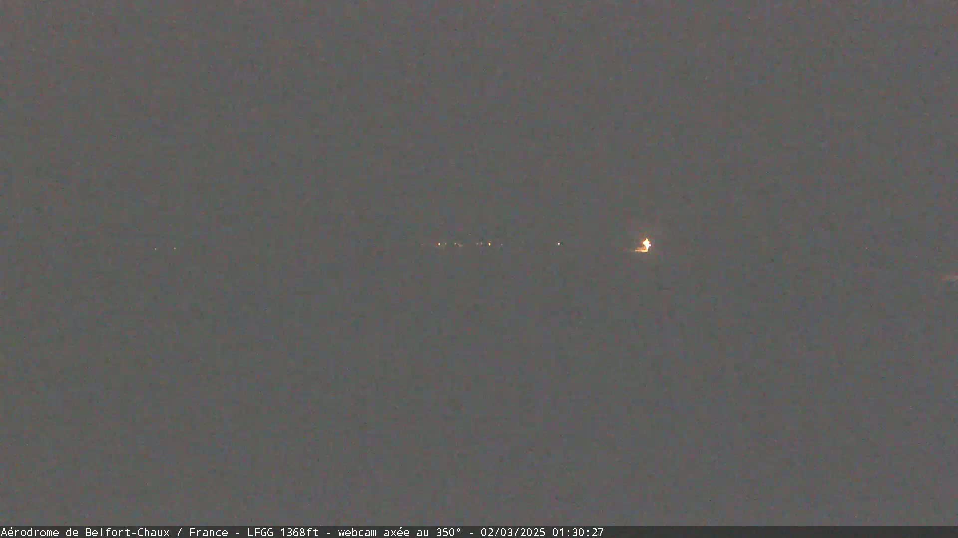 A dark, nighttime scene shows a few distant lights on the horizon under an overcast sky.