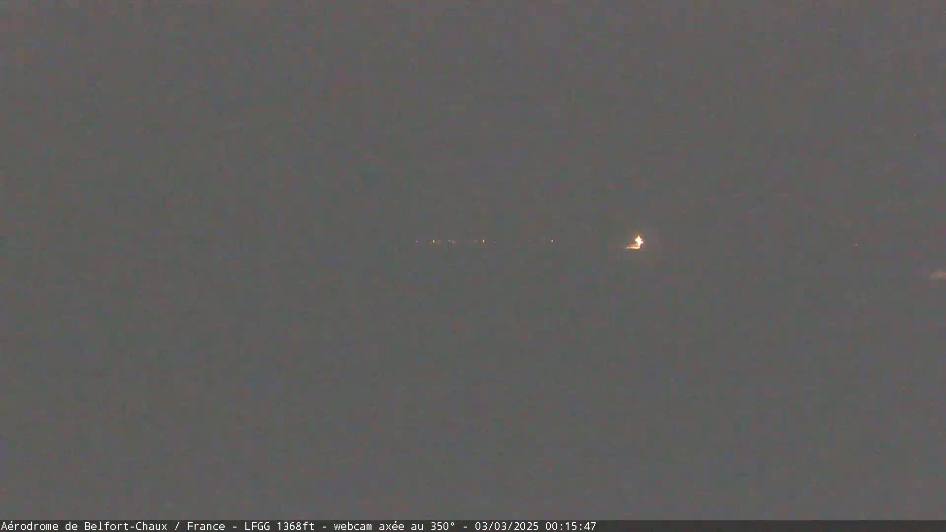 A dark, nighttime scene shows a few distant lights on the horizon under a dark sky.