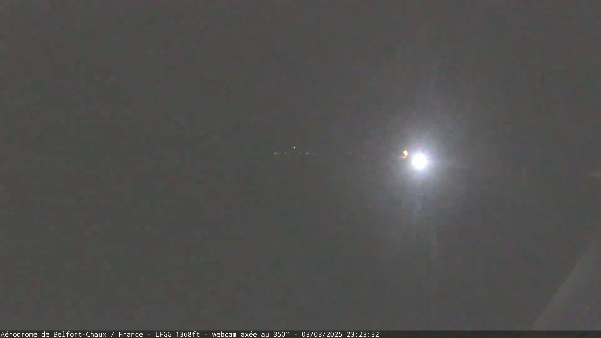 A bright light shines in the night sky above a dark, dimly lit landscape.