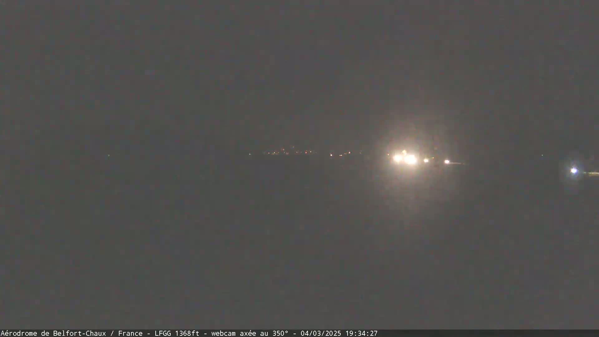 At night, a few distant lights are visible on a dark, flat landscape.