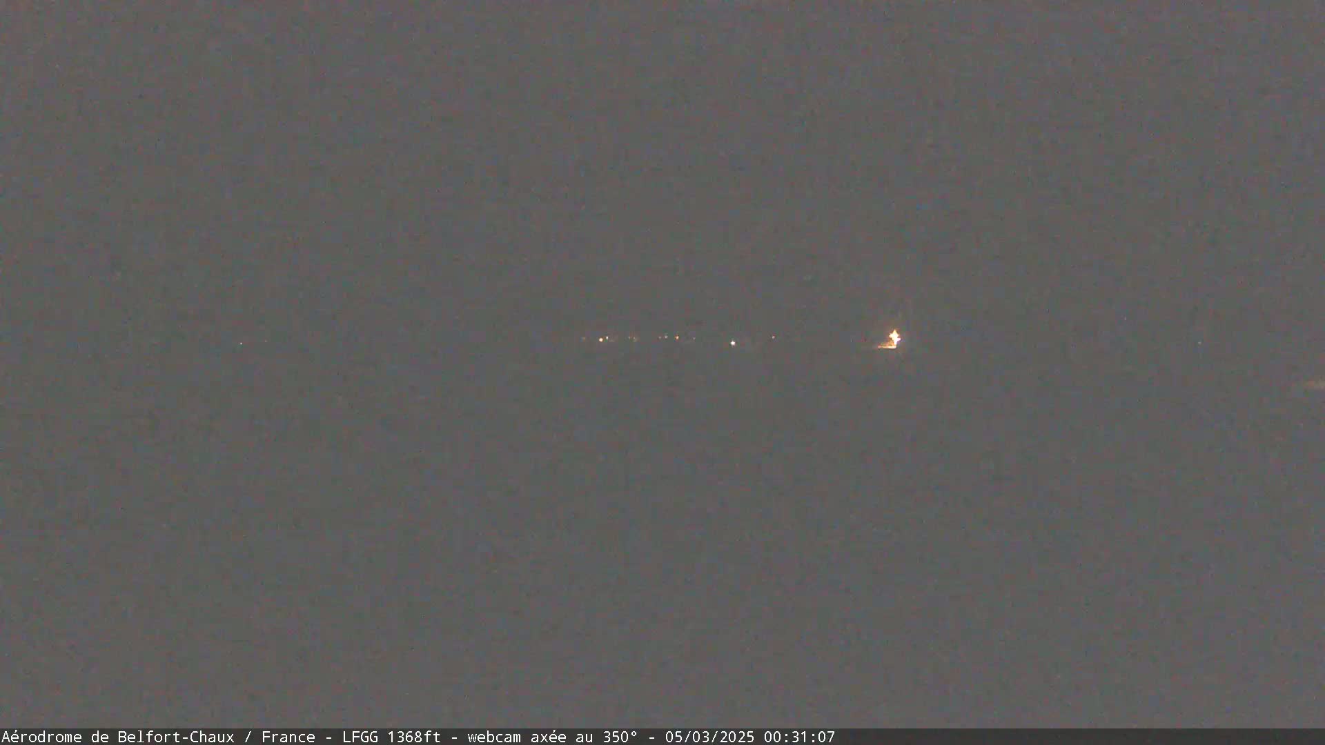 A long, dimly lit line of lights is visible at night in an otherwise dark, overcast scene.