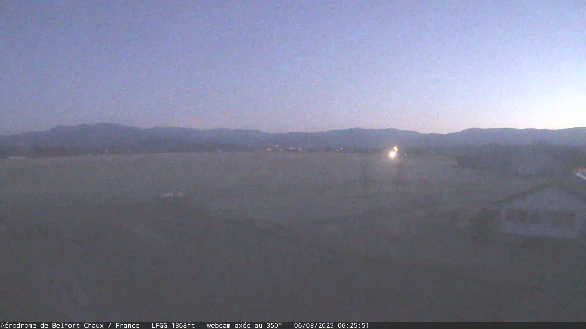 A flat, dimly lit landscape stretches out to distant, dark mountains under a twilight sky.