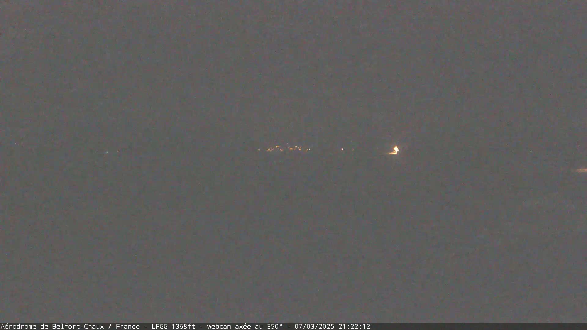 A dark, nighttime scene shows a distant line of faint lights, possibly a small town or village, under a clear, dark sky.