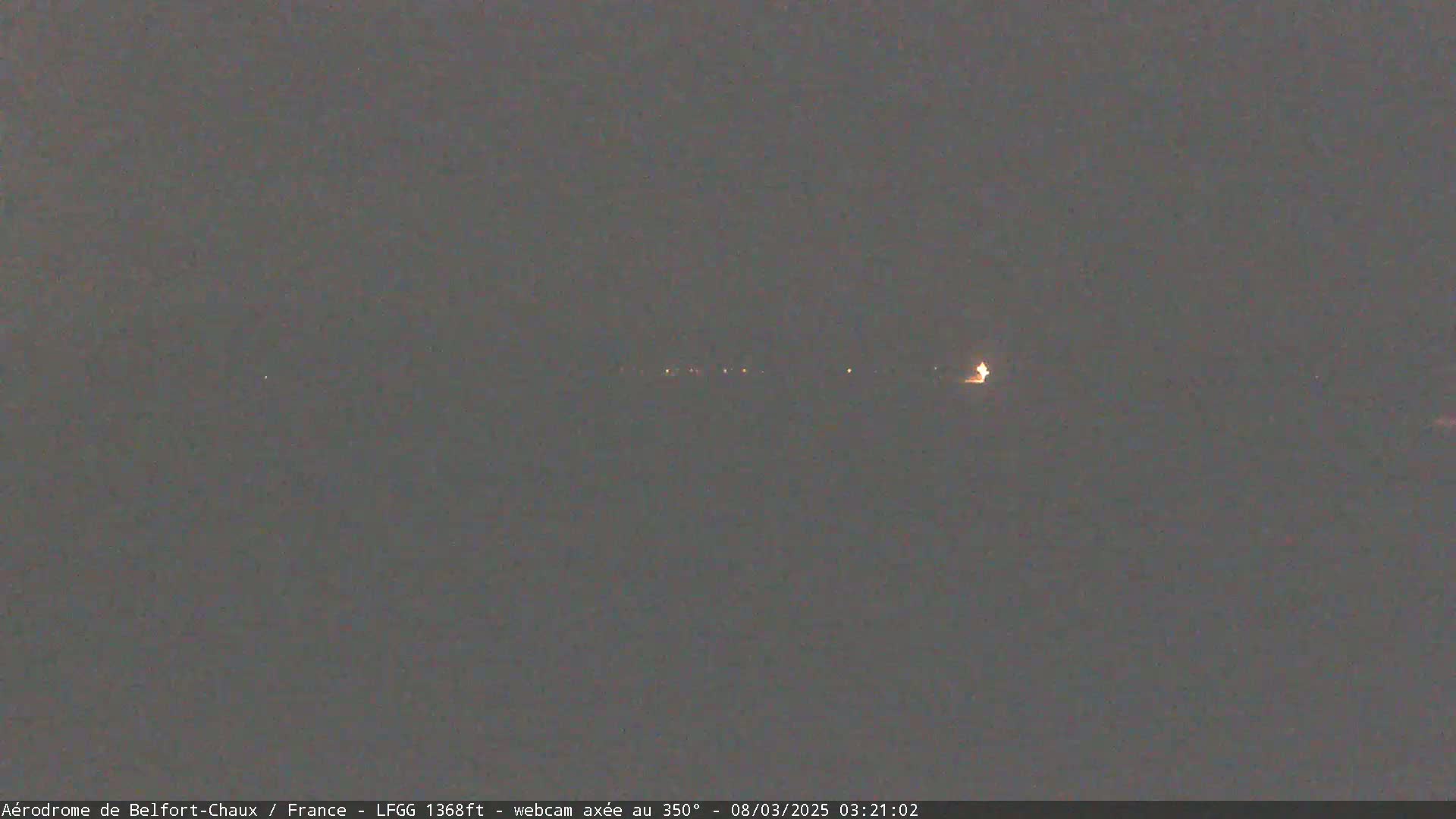 A dark, nighttime scene shows a line of distant lights on the horizon under a cloudy sky.