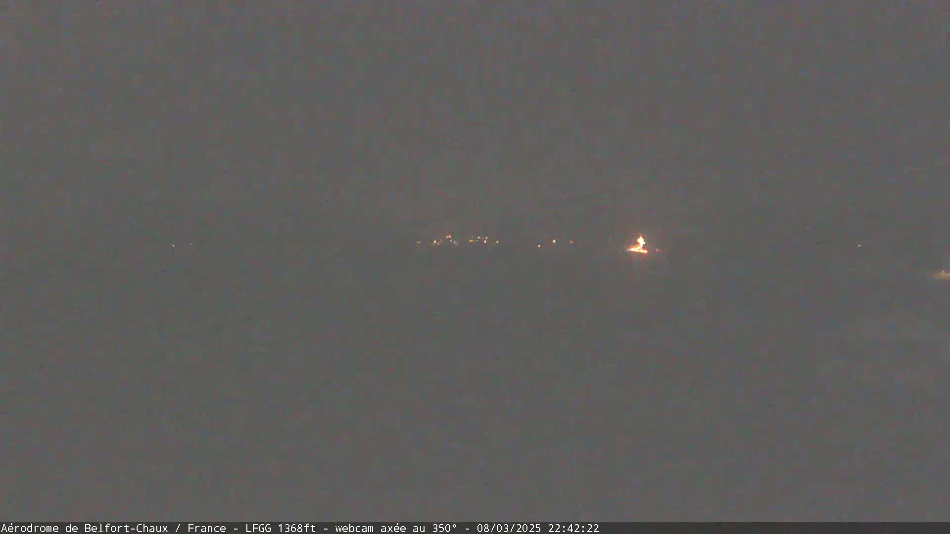 A nighttime, dark-gray landscape shows a distant line of faint lights under a mostly clear sky.