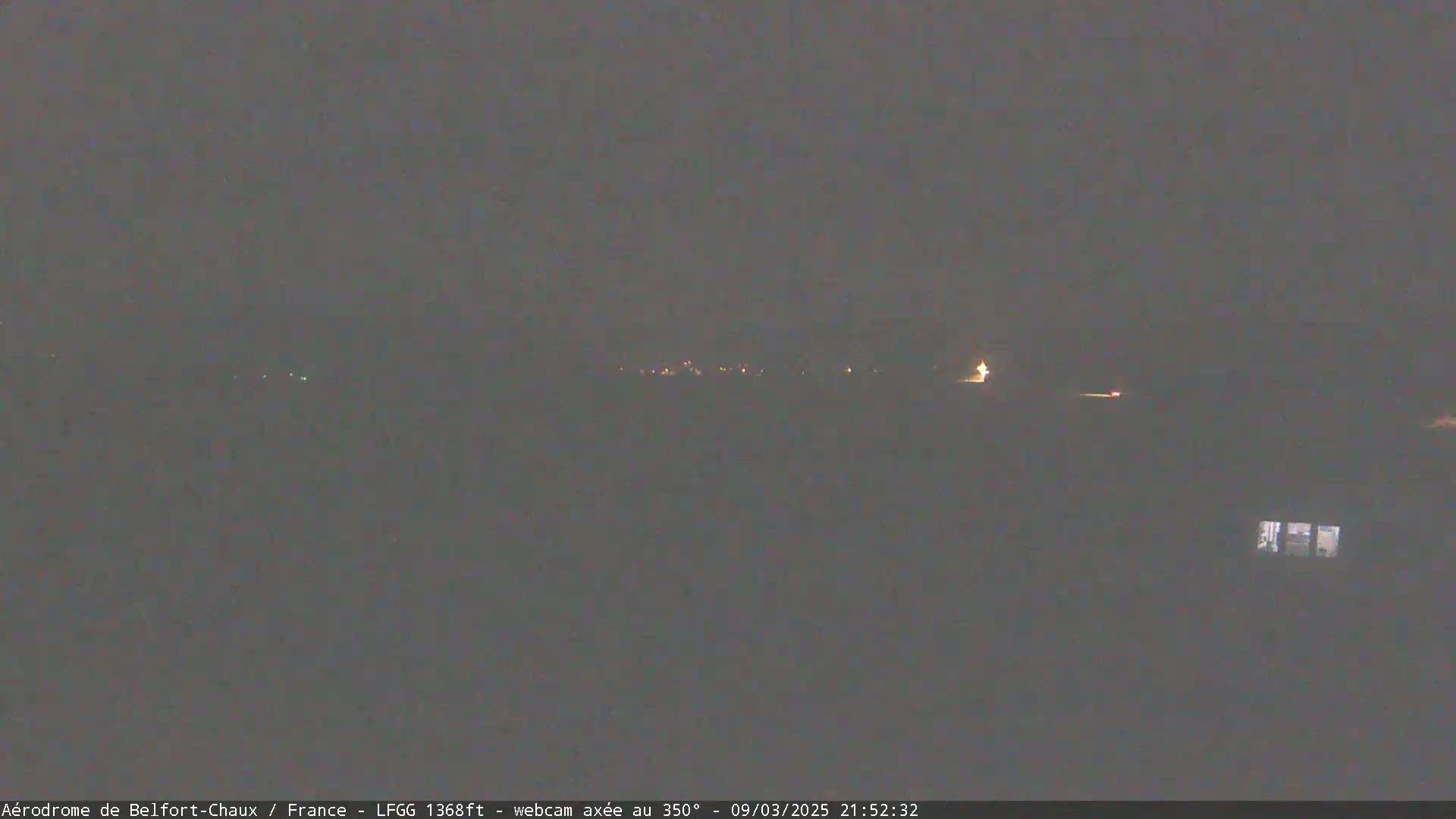 A dark, nighttime view of dimly lit buildings and lights in the distance under a cloudy sky.