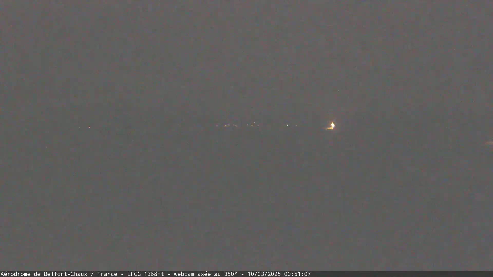 A dark, nighttime scene shows a dimly lit horizon with a few faint lights in the distance.