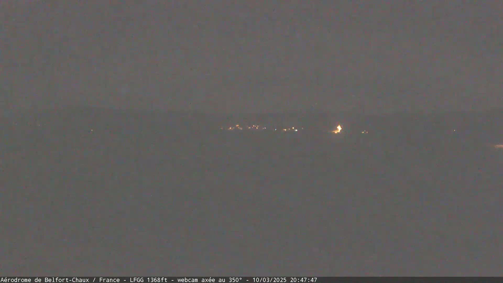 A dimly lit landscape at night is visible under a dark, overcast sky, showing a few distant lights.