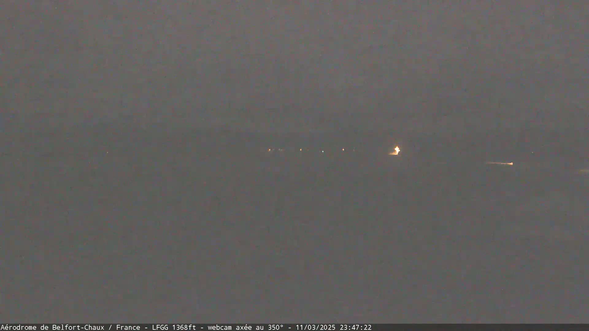 A dimly lit, nighttime landscape is visible, showing a few distant lights under an overcast sky.