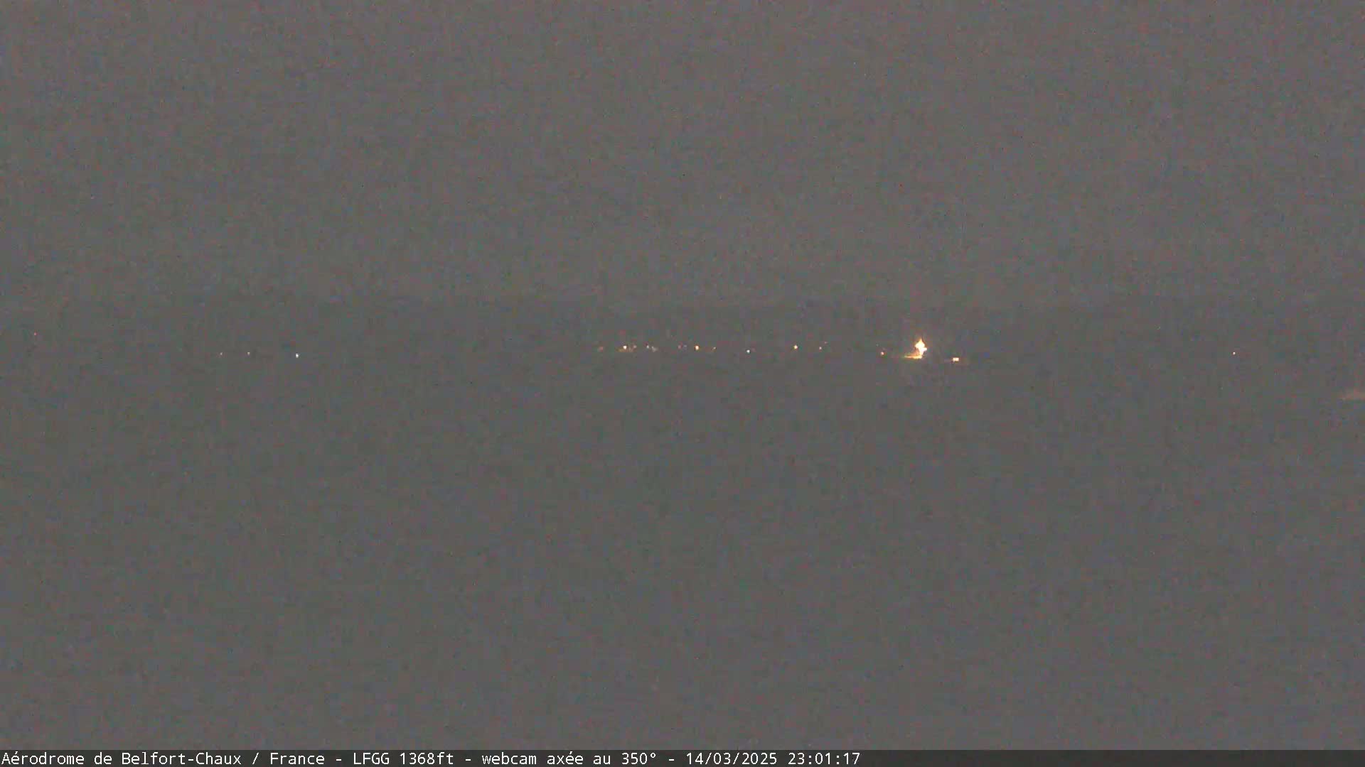 A nighttime, dark gray landscape shows a line of faint lights in the distance under a mostly clear sky.