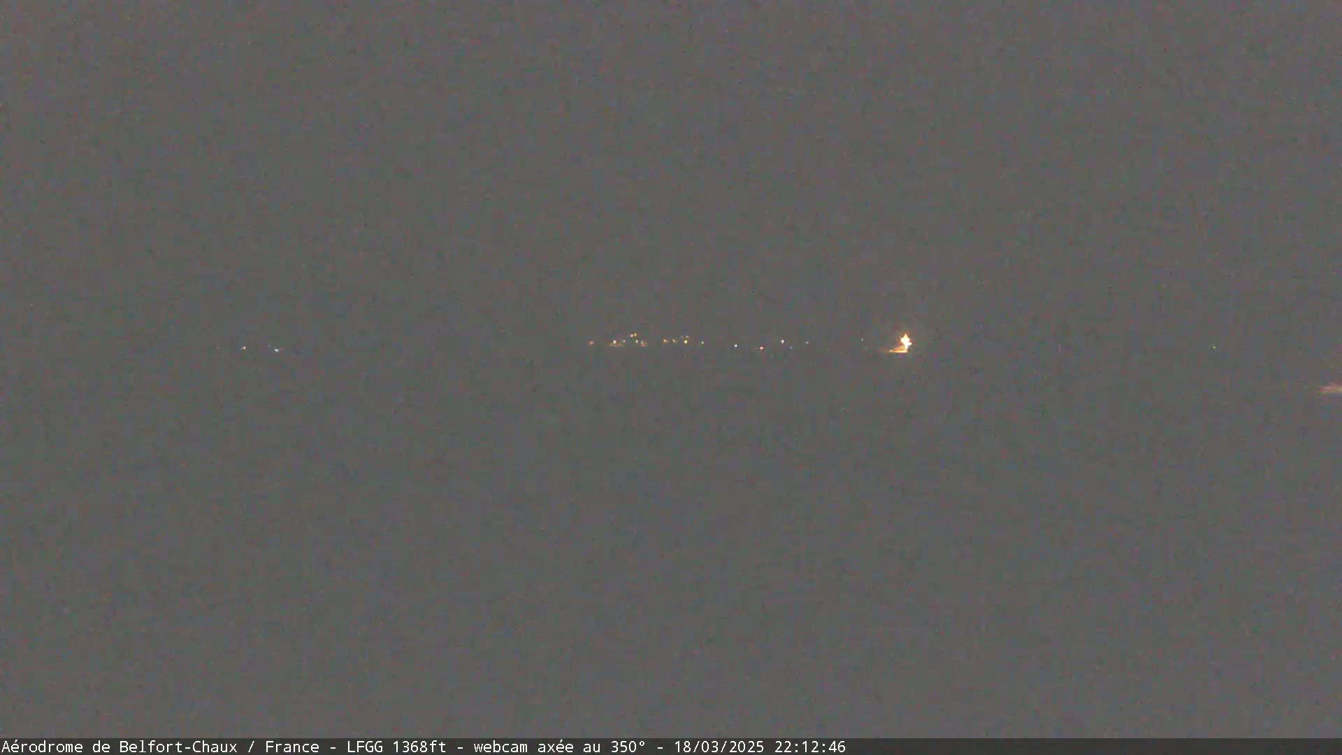 A dark, nighttime scene shows a line of faint lights in the distance under a clear, dark sky.
