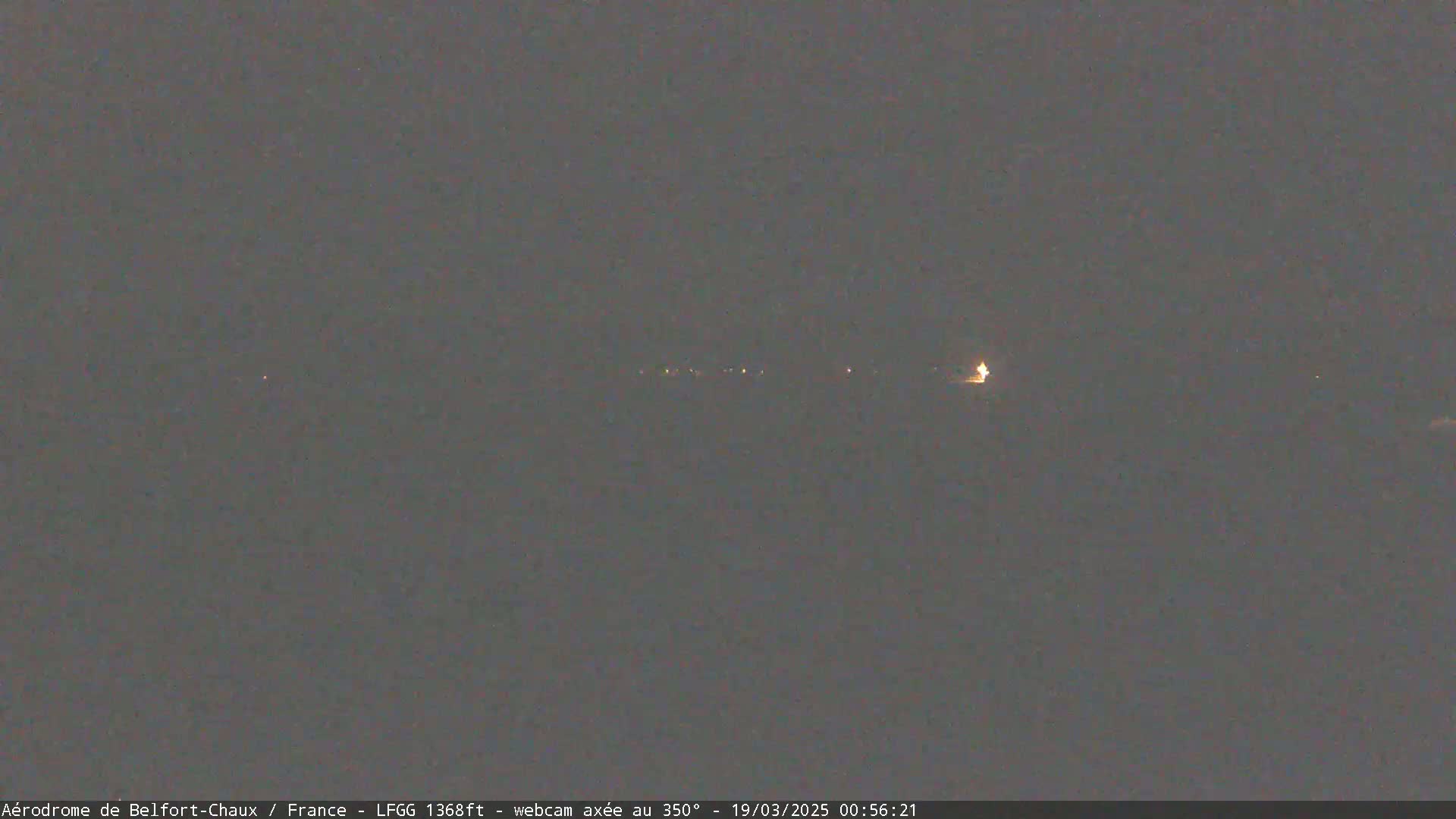 A nighttime, dimly lit landscape is visible, showing a faint line of lights in the distance under a dark sky.