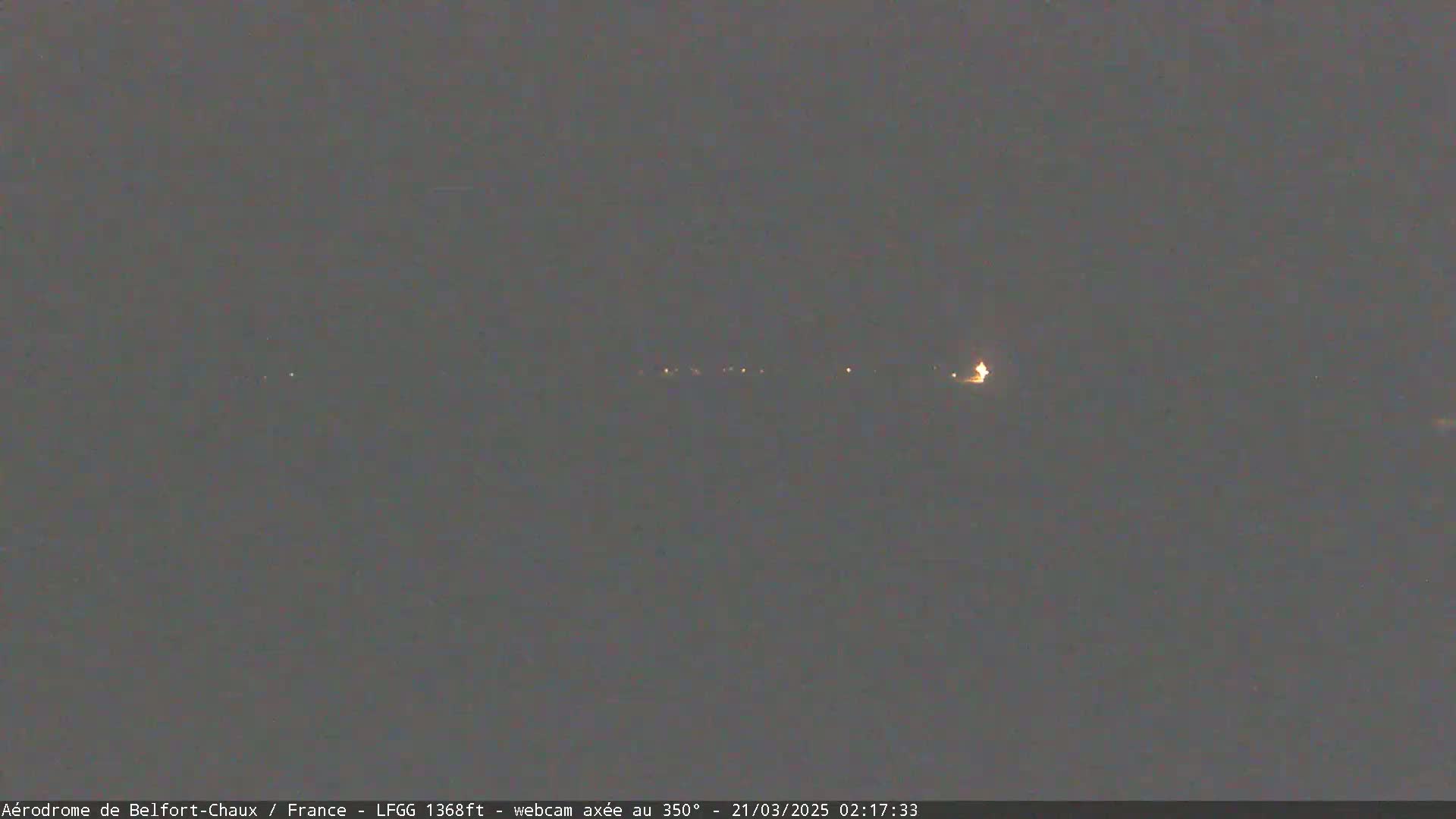 A dark, nighttime scene shows a line of faint lights in the distance under a clear, dark sky.