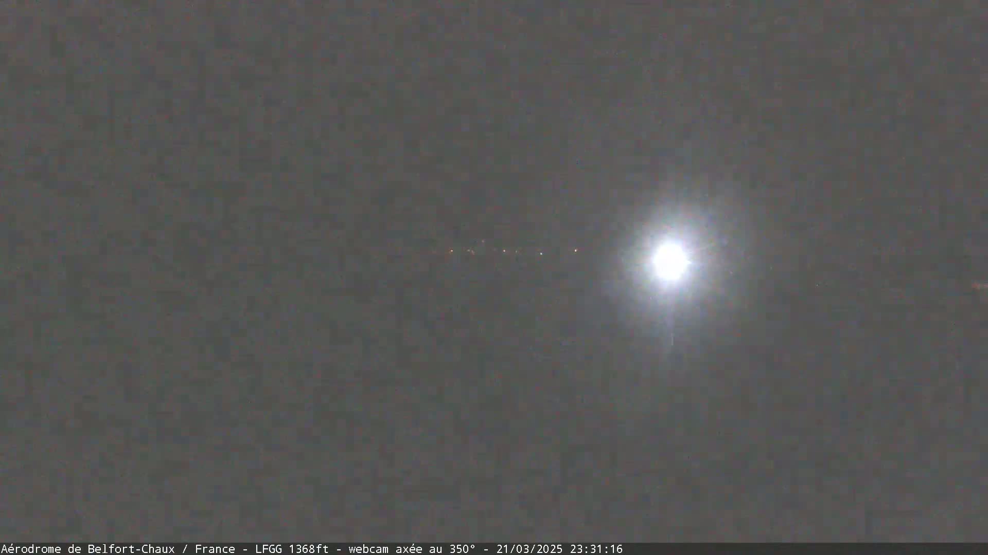 A bright light shines in a night sky over a dimly lit horizon.