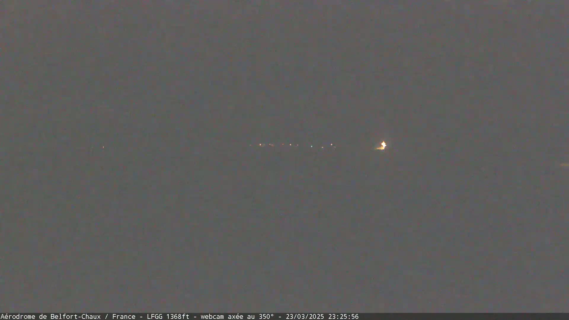 A dark, nighttime scene shows a few distant lights on the horizon under a cloudy sky.