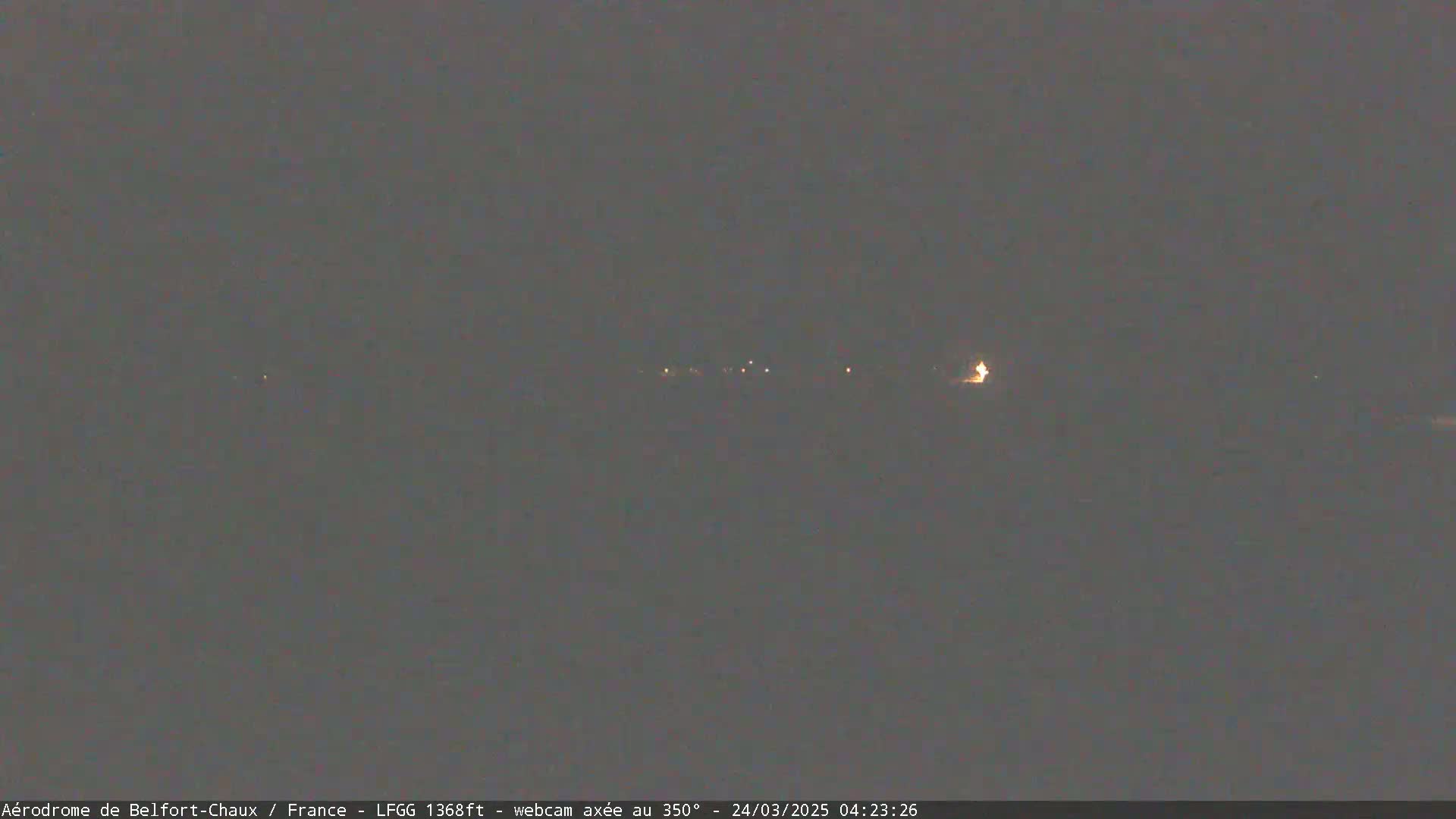 A dark, nighttime scene shows a faint line of distant lights under a gray sky.