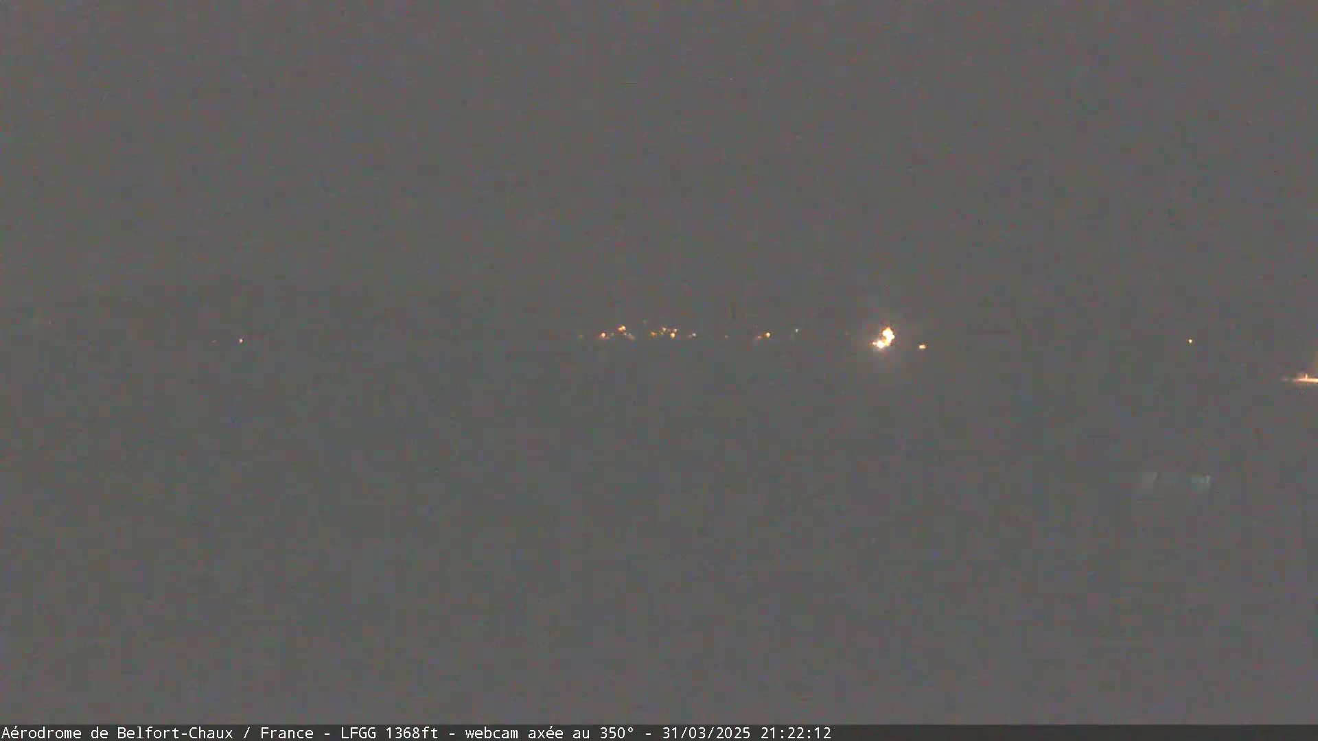 A dark, nighttime scene shows a distant line of faint lights, possibly a town or village, under a clear, dark sky.
