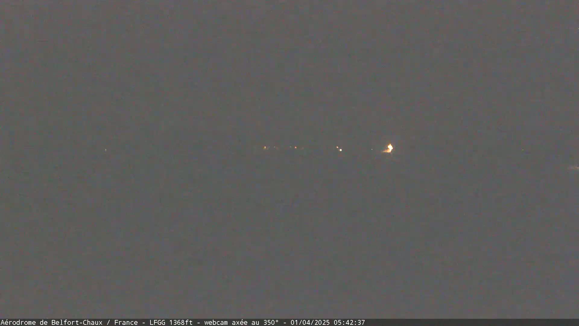 A dark, nighttime scene shows a few faint lights in the distance under a gray sky.