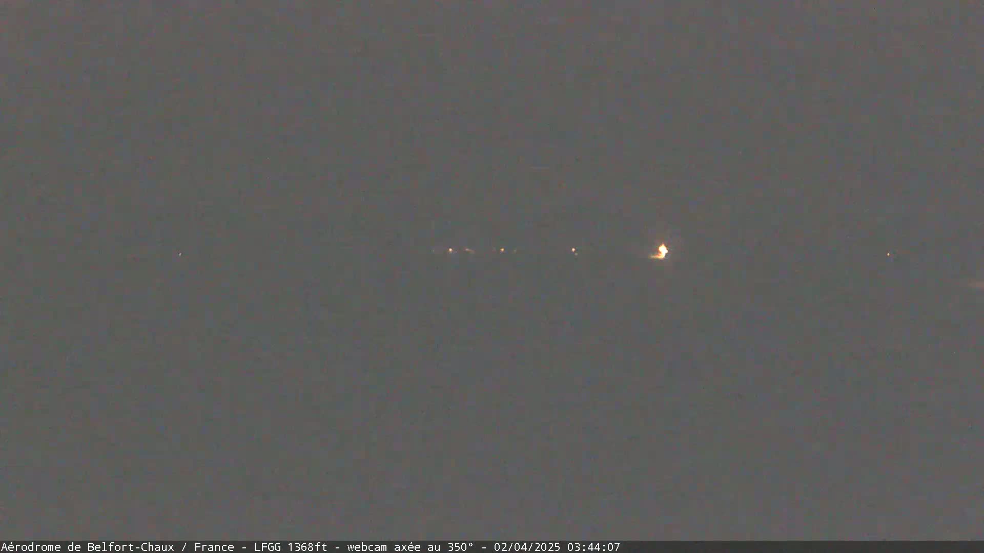 A dark, nighttime scene shows a few faint lights in the distance under a dark, overcast sky.
