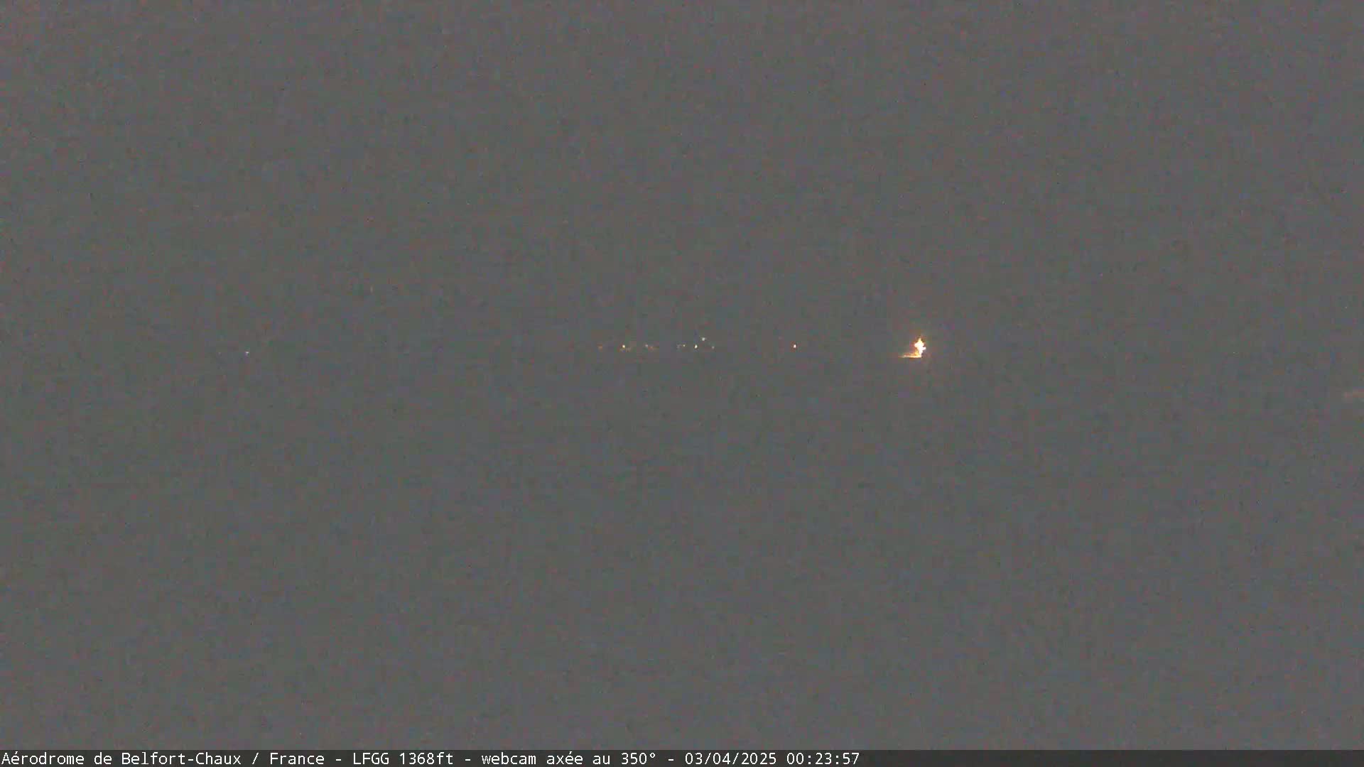 A nighttime long shot shows a dimly lit landscape with a few distant lights under a dark, overcast sky.