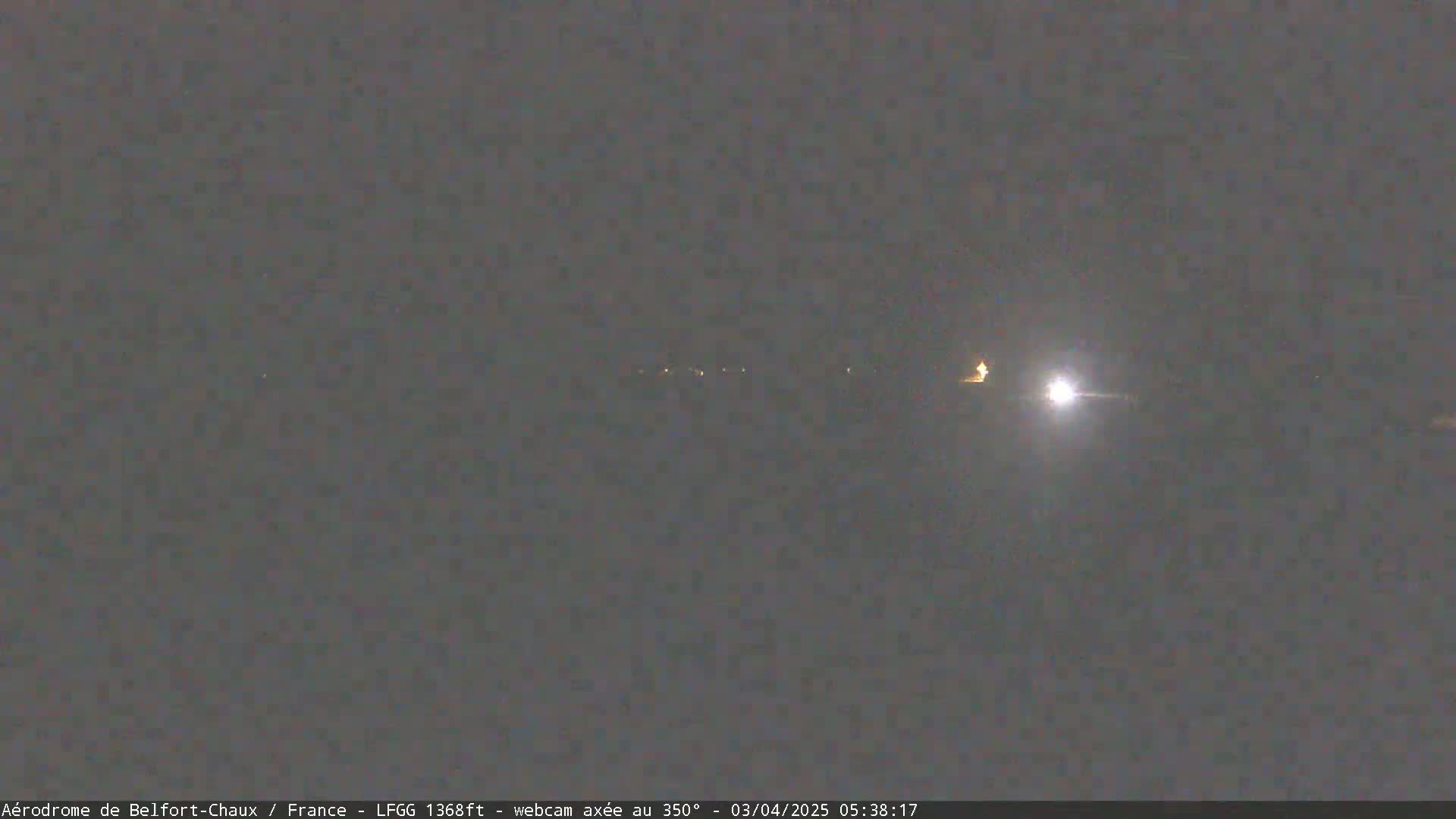 A nighttime, low-light image shows a distant line of lights and a bright light source possibly from a vehicle's headlights.