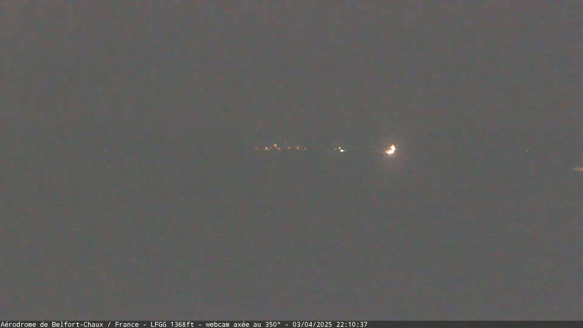 A nighttime long shot of dimly lit lights in the distance under a dark, overcast sky.