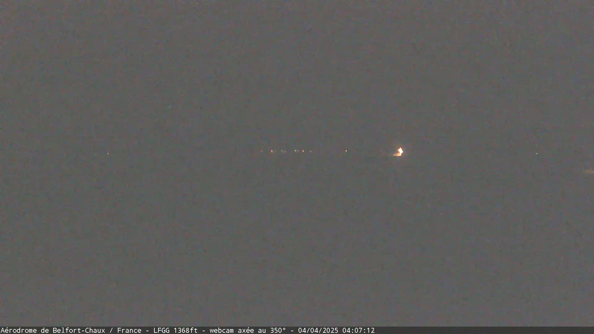 A dimly lit, nighttime scene shows a distant line of lights across a dark landscape.