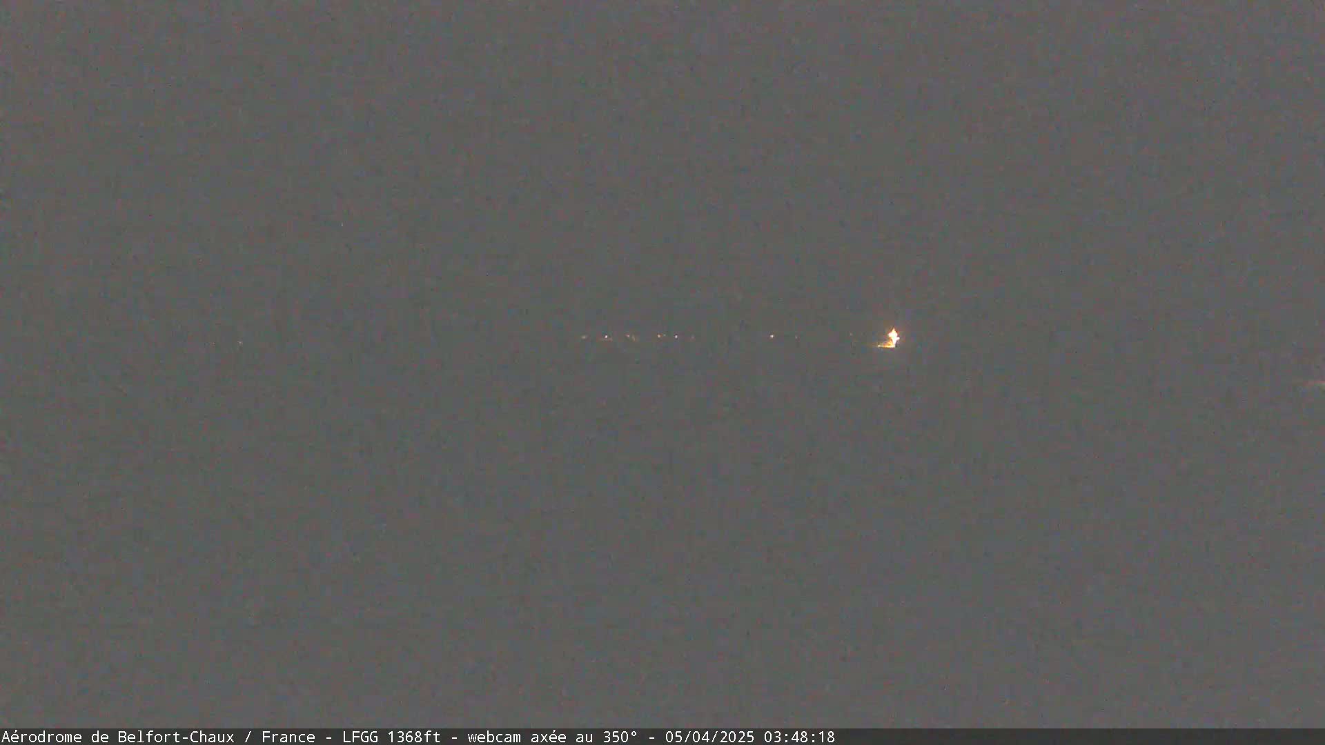 A dimly lit, dark gray landscape at night shows a line of faint lights in the distance.