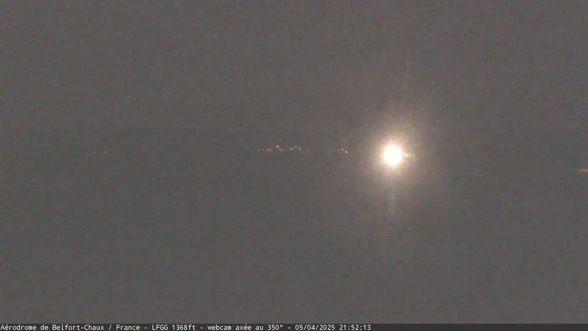 A bright light illuminates a dark, nighttime sky above a distant line of faint lights.