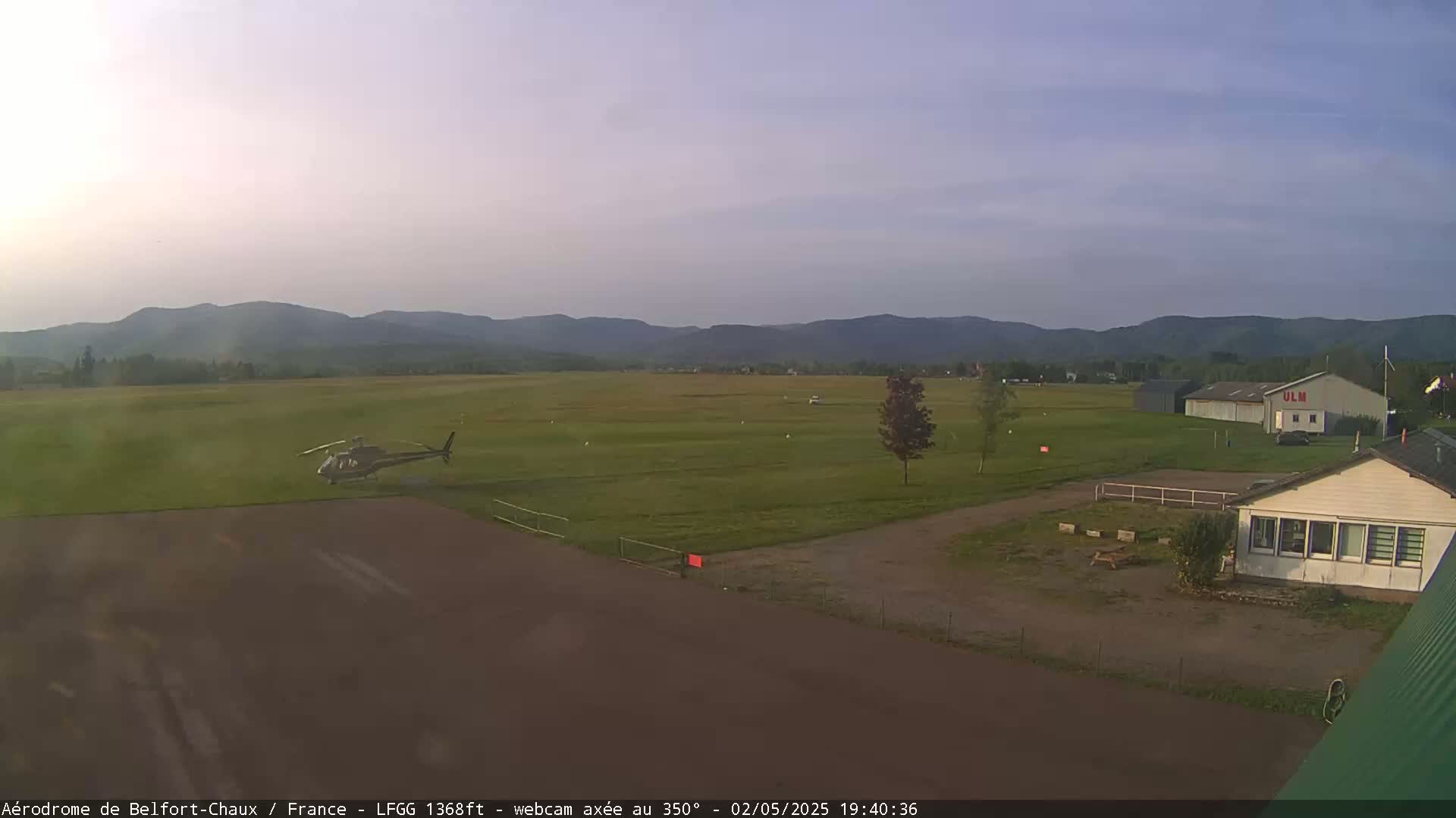 A helicopter is landing on a grassy airfield under a clear, twilight sky with mountains in the background.